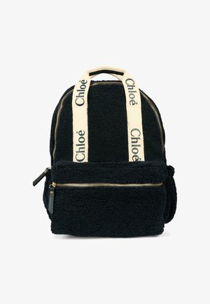 Zaino in pelliccia sintetica nera con dettagli in zip oro, dotato di spallacci crema contrassegnati "Chloé" e una tasca frontale con zip. Texture morbida.