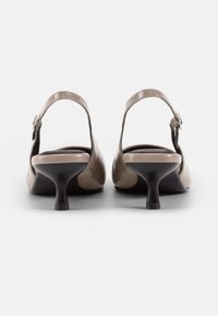 Beige patent leather slingback heels with a rounded toe, black rubber sole, and a low heel, featuring a silver buckle accent on the strap.