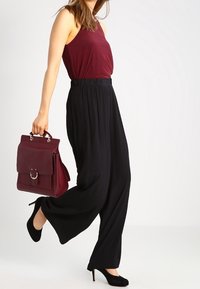 Burgundowy top na ramiączkach i czarne spodnie typu wide-leg. Uzupełniony burgundową torebką z okrągłym detalem metalowym. Czarne obcasy.