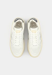 Sneakers in pelle bianca con dettagli perforati, suola crema e accenti grigi. Presentano lacci bianchi e un logo sulla linguetta.