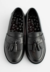 Mocassins en cuir noir avec des glands et des franges. L'intérieur présente un motif de cœurs sur fond noir. Design à bout rond et plat.