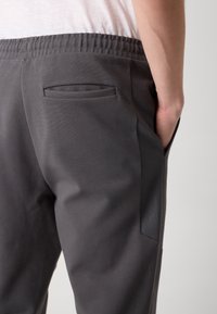 Pantaloni sport gri, cu o textură netedă, talie elastică și un buzunar pe partea din spate cu un model hexagonal subtil.