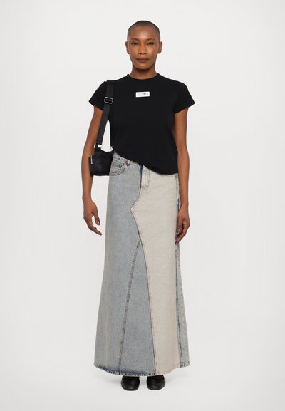 Black short-sleeve t-shirt with a logo, paired with a two-tone denim maxi skirt featuring an asymmetrical design and a dark bag worn crossbody.