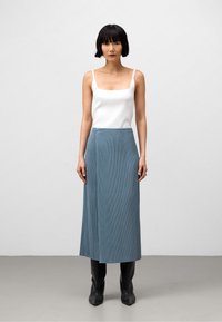 Vit fyrkantig ärm-topp kombinerad med en veckad blå midikjol, som har knäppning på sidan, och svarta knähöga stövlar.