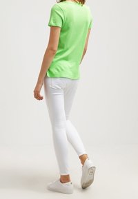 Grön bomullströja med kort ärm, ihop med vita slim-fit jeans och vita sneakers, visar en enkel, avslappnad outfit bakifrån.