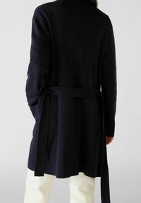 Marinblå stickad cardigan med långärmar och ett knytbälte i midjan. Har en ribbad textur och når till mitten av låret.