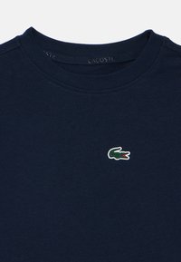 Námořnická modrá bavlněná trička s kulatým výstřihem, na přední straně s malým vyšitým logem krokodýla v zelené, bílé a červené barvě.