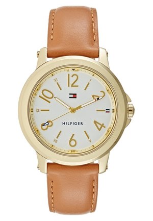Gold-tone Tommy Hilfiger watch with white dial, tan leather strap, gold numerals, and logo at center, showing time 10:10:40.