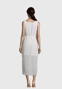 Vestido blanco sin mangas con cintura ajustada, parte inferior transparente y textura plisada, que llega a mitad de pantorrilla. Se lleva con zapatos de tacón nude.
