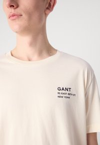 Lichtcreme kortemouw T-shirt van zacht katoen, met geborduurde tekst "GANT 32 EAST 39TH ST. NEW YORK" in marineblauw op de borst.