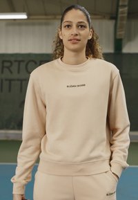 Felpa beige con scollatura rotonda, maniche lunghe e polsini a coste. Presenta il logo "BJÖRN BORG" in verde scuro sul petto.