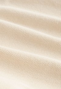 Tissu beige texturé avec un motif côtelé diagonal, présentant des fibres douces et lisses ainsi que de légères variations de teinte sur toute la surface.