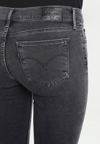 Jeans de mezclilla gris oscuro con un diseño ajustado, que cuentan con un bolsillo trasero distintivo con un detalle de costura curva y una etiqueta de cuero negro en la cintura.