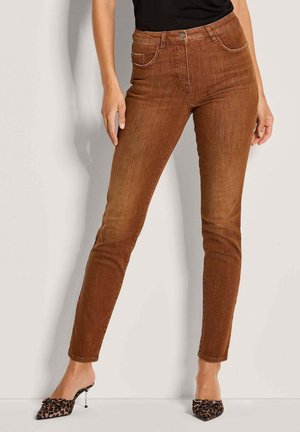 Braune enge Jeans aus Denim mit fünf Taschen, einem Knopf- und Reißverschluss und dezentem Verblassen. Getragen mit schwarzen Mules im Leopardenmuster.
