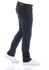 Jeans de mezclilla negra con corte ajustado, cinco bolsillos y una etiqueta de la marca en la parte posterior de la cintura. Combinados con zapatillas blancas. Textura suave.