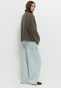 Olivengrüner Strickpullover mit Rollkragen und lockerem Schnitt, kombiniert mit hellblauen, oversized Jeans. Mit gerippten Bündchen und Saum.