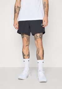 Svarta sportshorts med Nike-logotyp, kombinerat med vita ankelsockor med Nikes logotyp och vita sneakers. Tatueringar synliga på benen.