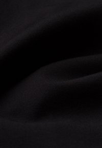 Mustaa kangasta, jossa on sileä, hieman teksturoitu pinta, hienovarainen venyvyys ja tasainen väri, joka esittää pehmeitä taitoksia ja roikkuvuutta.