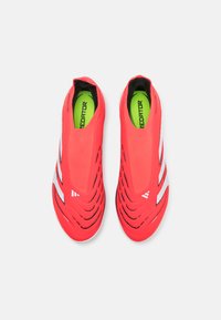 Red soccer shoes with a smooth upper, featuring cut-out grooves, white stripes, and bright green insoles, designed for agility and comfort.