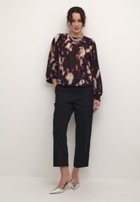 Transparent, mörklila blus med abstrakta mönster, ballongsärmar; matchad med svarta skräddarsydda byxor och silverfärgade spetsiga klackskor.