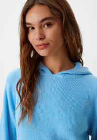 Hellblaues Kapuzensweatshirt mit gerippter Textur, das einen lässigen Schnitt und ein leicht übergroßes Design aufweist. Weicher Stoff mit sichtbaren Nähdetails.
