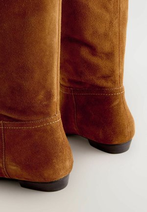 Braune Wildleder-Stiefel in Knielänge mit enganliegendem Design, sichtbaren Nähdetails, einem kleinen Absatz und einer glatten Oberflächenstruktur.
