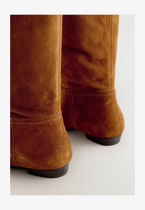 Hnedé semišové čižmy po kolená s priliehavým strihom, viditeľnými švami, malým podpätkom a hladkým povrchom.