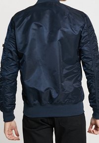 Chaqueta bomber azul marino con un exterior liso y brillante. Presenta puños y dobladillo acanalados, y detalles fruncidos en las mangas.