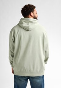 Sudadera verde claro con cordón, de corte relajado y mangas largas, combinada con jeans azules. La tela parece suave y texturizada.
