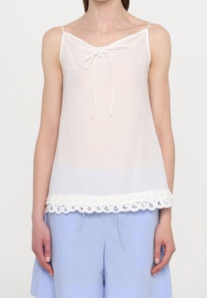 Donna che indossa un top bianco senza maniche con dettaglio annodato e rifinitura in pizzo, abbinato a pantaloncini larghi azzurri.