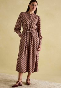 Langärmliges Kleid mit floralem Muster in rosa und lila Tönen, mit tailliertem Schnitt und gerafften Ärmeln, kombiniert mit bordeauxfarbenen Mary Jane Schuhen.