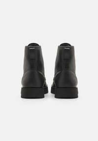 Schwarze Leder-Stiefeletten mit glatter Oberfläche, runder Zehenform und einer stabilen, niedrigen schwarzen Sohle. Die Rückansicht hebt das minimalistische Design hervor.