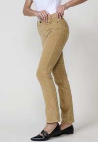 Tan corduroy broek met een slim fit, voorzien van voorzakken, riemlussen en een soepele textuur. Draag met zwarte platte schoenen.