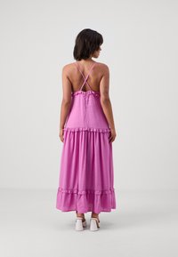 Rochie maxi roz cu bretele subțiri, accente volan la decolteu și la tiv, și o croială lejeră. Țesătura are o textură moale și o strălucire subtilă.