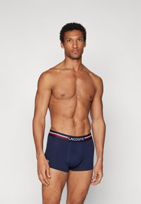 Marineblå bomullsboxer med en kontrasterende stripet linning som har Lacoste-logoen. Glatt tekstur og tettsittende design.