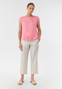 Lichtroze, kortearmige top in combinatie met beige, losse, cropped broek. Model draagt beige sandalen met een geweven band. Soepele structuur.