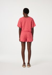 Koraalkleurige katoenen twee-delige outfit met broderie anglaise details. Korte mouwen en gegolfde randen op zowel de top als de shorts.