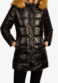 Manteau en duvet noir avec une finition brillante, muni d'une capuche en fausse fourrure amovible, d'une fermeture éclair à l'avant et de deux poches latérales. Les coutures créent un design matelassé.