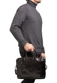 Sac à ordinateur portable en cuir noir avec deux poignées, fermeture éclair et une bandoulière amovible, présenté sur un fond uni.