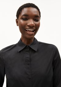 Black button-up shirt with a structured collar, smooth texture, and long sleeves; features visible buttons and a minimalist design.