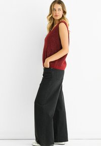 Red sleeveless knit top with a v-neckline, paired with high-waisted black wide-leg jeans. The outfit features a relaxed fit and textured fabric.