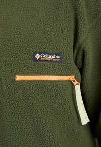 Oliven grøn fleecejakke med tekstureret overflade, en lynlås lomme med en orange lynlås og et marineblåt logo-patch fra Columbia Sportswear.