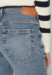 Light blue denim jeans with a high-waisted fit, featuring contrasting orange stitching and a brown leather brand tag on the back.