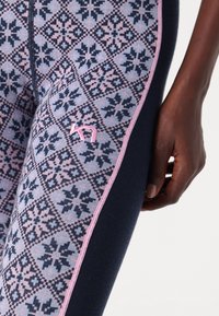 Tights gjorda av sträckbart material med ett geometriskt mönster av rosa och blå snöflingor, med mörknavy sidor och en rosa logotyp.