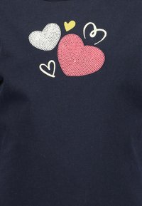 T-shirt blu navy con design di cuori multicolori: un cuore a pois bianchi, un cuore rosa testurizzato e un piccolo contorno di cuore giallo.