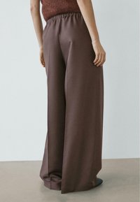 Hnědé široké kalhoty s elastickým pasem, s hladkou texturou a pohodlným střihem, focené zezadu.