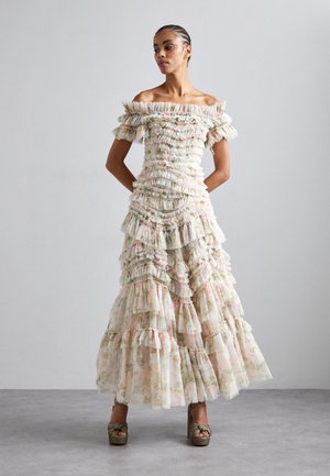 Mekko, jossa on paljaat hartiat ja röyhelöitä, vaaleassa kukkakirjailussa. Sisältää useita kerroksia ja tekstuuritarkkuuksia, yhdistettynä kimalteisiin alustossandaaleihin.