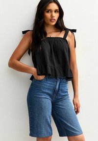 Svart kort topp med volangkant och axelband, kombinerad med knä-långa blå denimshorts. Slät textur med en avslappnad passform.