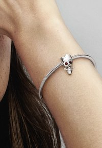 Bracciale in argento con un design texture e un charm che ricorda un piccolo personaggio, con occhi rossi e un volto dettagliato.