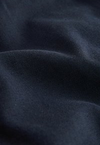 Tamno plava tkanina s teksturiranim, tkanim izgledom, koja prikazuje suptilne uzorke i varijacije u nijansama po površini.